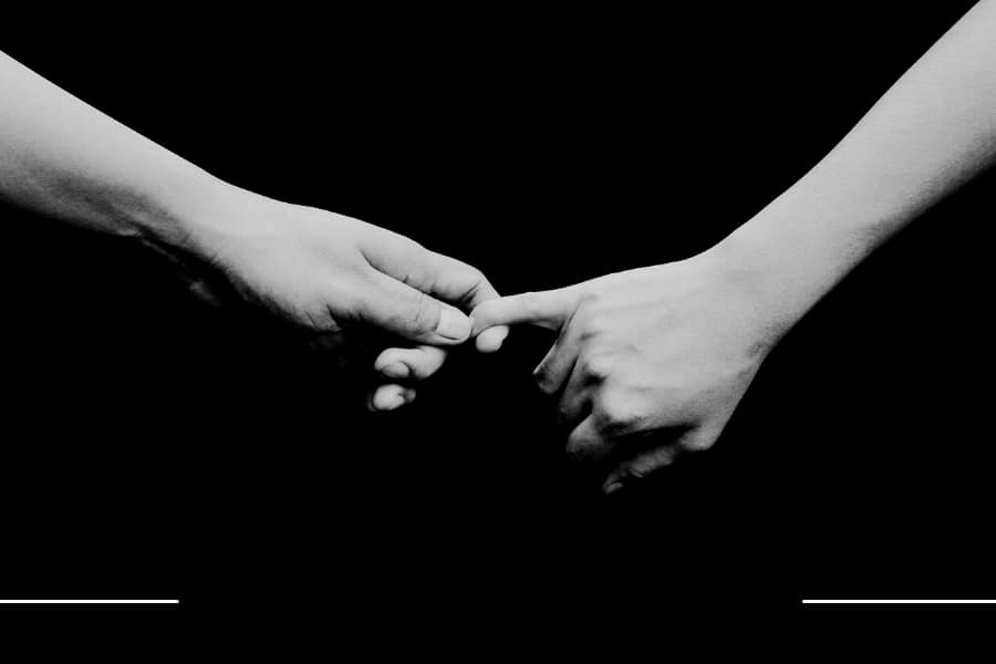 A hand holding another hand by the pinky finger with black background.